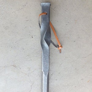 May include: A twisted metal rod with a leather strap attached to the top. The rod is silver in color and has a pointed end.