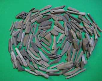 May include: A collection of weathered driftwood pieces in various shapes and sizes, arranged on a green background. The wood tones range from light gray to dark brown, with visible textures and natural imperfections. The arrangement suggests a craft or decorative theme.