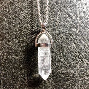 May include: A silver chain necklace with a clear quartz crystal pendant. The crystal is shaped like a point and is held in a silver setting.