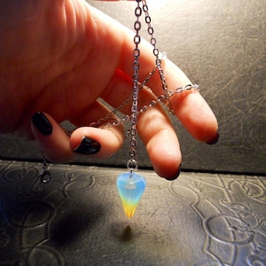 Puede incluir: Un collar de cadena plateada con un colgante en forma de lágrima. El colgante está hecho de ópalo iridiscente con colores azul, amarillo y blanco.