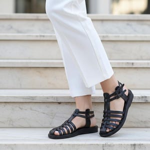Elegant black leather gladiator sandals walking down marble stairs. Classic women's handmade summer shoes offering chic comfort for formal or casual wear.