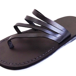 May include: Black leather sandals with multiple straps across the foot. The sandals have a simple design and a flat sole.