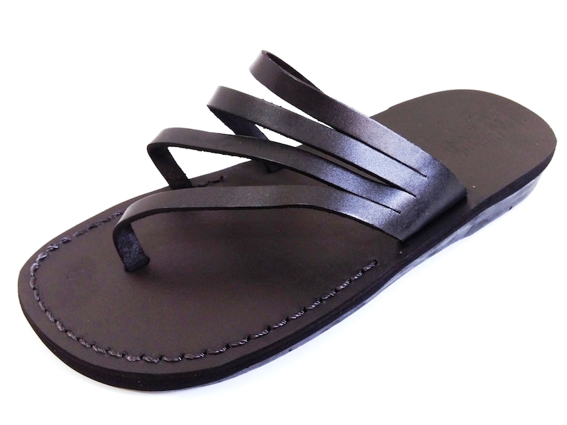 May include: Black leather sandals with multiple straps across the foot. The sandals have a simple design and a flat sole.