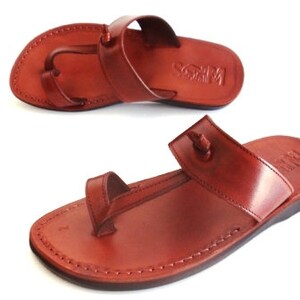 K&ouml;nnte beinhalten: Ein Paar braune Ledersandalen mit einem Zehensteg und einem Kn&ouml;chelriemen. Die Sandalen haben ein schlichtes Design und sind aus hochwertigem Leder gefertigt.