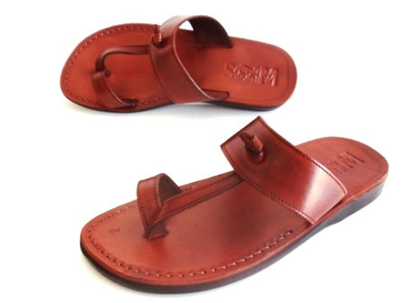 K&ouml;nnte beinhalten: Ein Paar braune Ledersandalen mit einem Zehensteg und einem Kn&ouml;chelriemen. Die Sandalen haben ein schlichtes Design und sind aus hochwertigem Leder gefertigt.