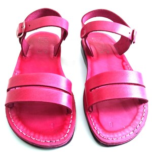 May include: A pair of pink leather sandals with an ankle strap and buckle fastening. The sandals have a simple design with a single strap across the toe.