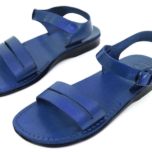 May include: A pair of blue leather sandals with adjustable ankle straps. The sandals have a simple design with a single strap across the top of the foot.