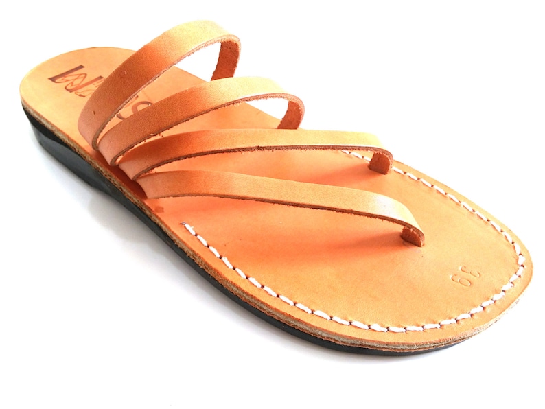 May include: Tan leather sandals with multiple straps and a white stitched sole. The sandals have a simple design and are made of high-quality leather.