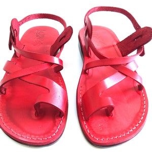 K&ouml;nnte beinhalten: Ein Paar rote Ledersandalen mit gekreuzten Riemen und einem Kn&ouml;chelriemen.