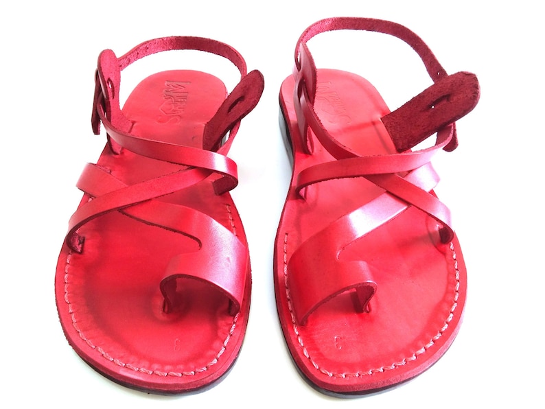 K&ouml;nnte beinhalten: Ein Paar rote Ledersandalen mit gekreuzten Riemen und einem Kn&ouml;chelriemen.