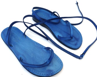 Può includere: Un paio di sandali in pelle blu con lacci che si legano alle gambe. I sandali hanno un design semplice e sono realizzati in pelle morbida.