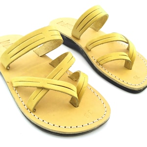 May include: A pair of tan leather sandals with multiple straps. The sandals have a simple design and are perfect for warm weather.