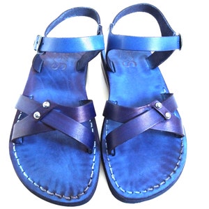 May include: A pair of blue leather sandals with a cross-strap design. The sandals have adjustable ankle straps and are stitched with white thread. The leather has a gradient effect, transitioning from a lighter to a darker shade of blue.
