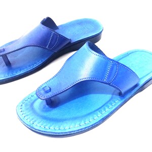 Peut inclure: Une paire de sandales en cuir bleu avec un design simple. Les sandales ont une seule sangle sur le dessus du pied et une boucle pour les orteils.