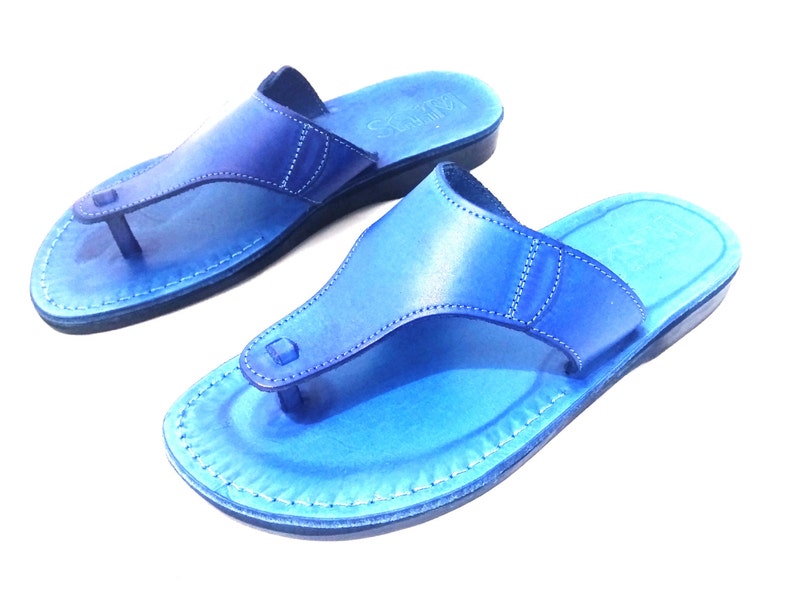 Peut inclure: Une paire de sandales en cuir bleu avec un design simple. Les sandales ont une seule sangle sur le dessus du pied et une boucle pour les orteils.