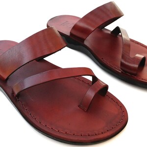 May include: A pair of brown leather sandals with a toe loop and two straps. The sandals have a simple design and are made of high-quality leather.