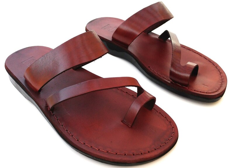 May include: A pair of brown leather sandals with a toe loop and two straps. The sandals have a simple design and are made of high-quality leather.