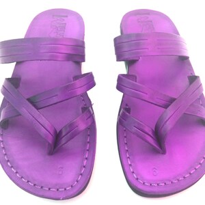 May include: A pair of purple leather sandals with criss-cross straps. The sandals have a simple design and are made of high-quality leather.