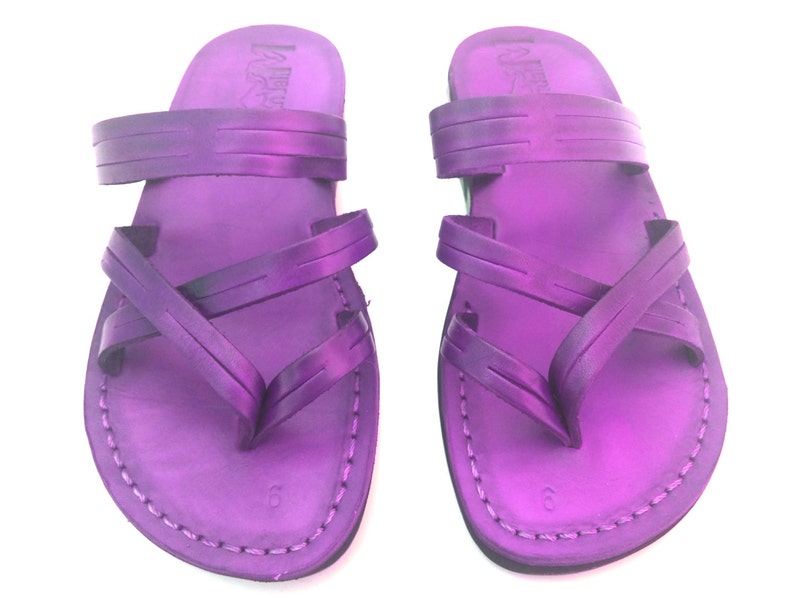 May include: A pair of purple leather sandals with criss-cross straps. The sandals have a simple design and are made of high-quality leather.
