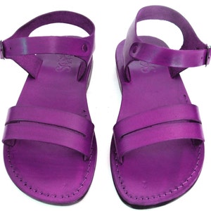 May include: A pair of purple leather sandals with an ankle strap and buckle closure. The sandals have a simple design with a single strap across the top of the foot.
