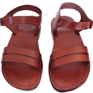 May include: A pair of brown leather sandals with ankle straps. The sandals have a simple design with two straps across the top of the foot.