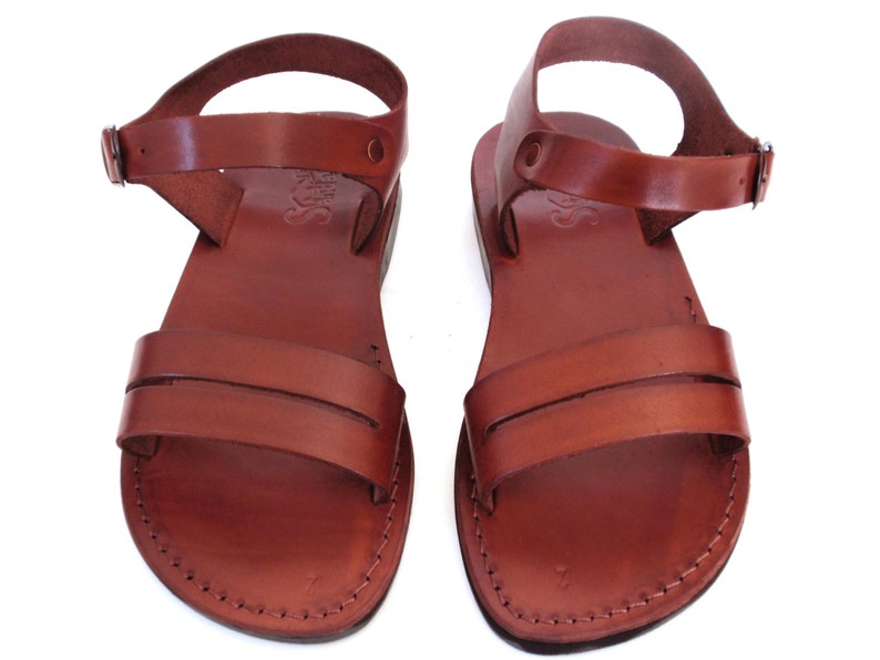 May include: A pair of brown leather sandals with ankle straps. The sandals have a simple design with two straps across the top of the foot.