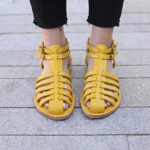 Mustard yellow handmade leather sandals viewed from above on pavement. Vibrant strappy gladiator flats adding color to comfortable women's summer style.