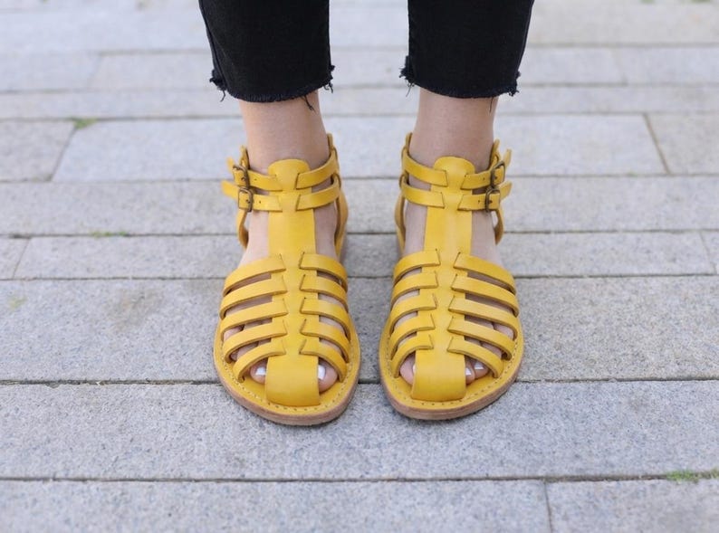 Mustard yellow handmade leather sandals viewed from above on pavement. Vibrant strappy gladiator flats adding color to comfortable women's summer style.