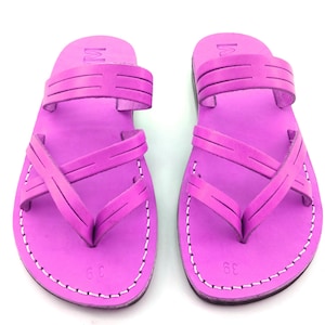 May include: A pair of bright pink leather sandals with criss-cross straps and a simple design. The sandals have a white stitch detail around the edges.