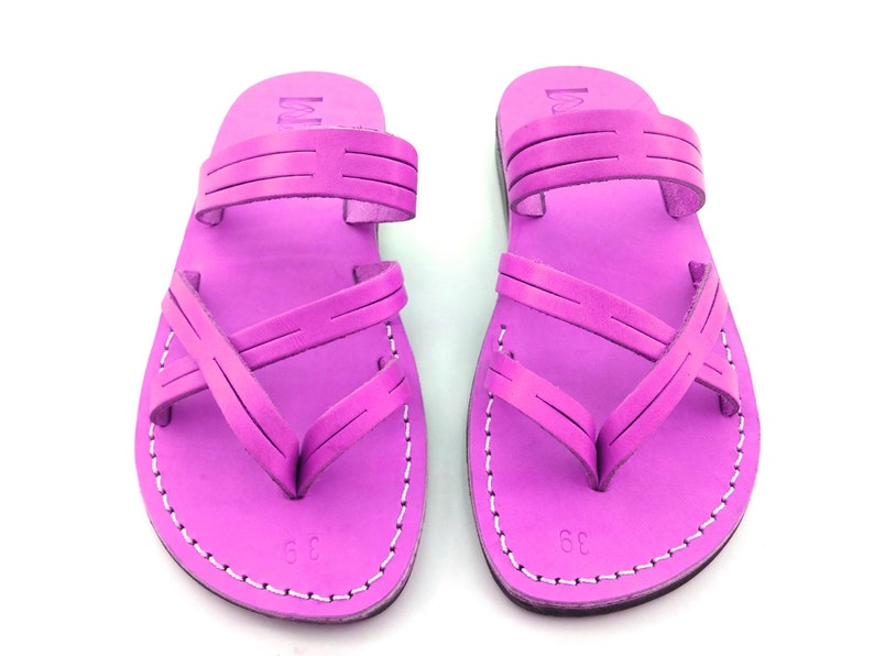 May include: A pair of bright pink leather sandals with criss-cross straps and a simple design. The sandals have a white stitch detail around the edges.