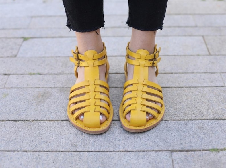 Mustard yellow handmade leather sandals viewed from above on pavement. Vibrant strappy gladiator flats adding color to comfortable women's summer style.