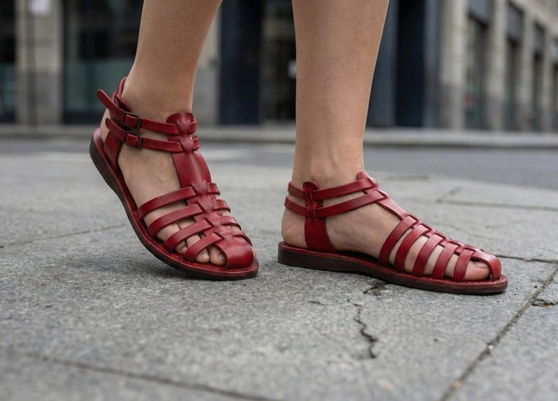 Deep red handmade leather gladiator sandals walking on a city street. Comfortable women's strappy summer shoes with durable flat soles for travel.