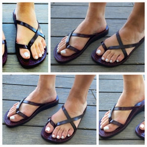May include: Brown leather sandals with criss-cross straps and a thong toe. The sandals have a flat sole and are shown being worn by a person.
