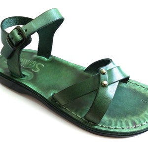 May include: Green leather sandal with an ankle strap and buckle closure. The sandal features a cross-strap design across the foot and is stitched around the edges. The sole is black, and the sandal has a distressed finish.