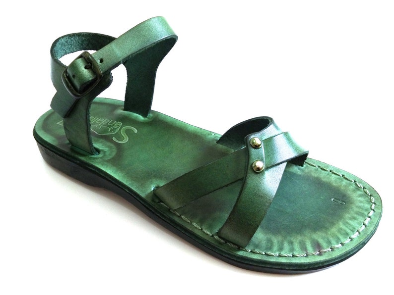May include: Green leather sandal with an ankle strap and buckle closure. The sandal features a cross-strap design across the foot and is stitched around the edges. The sole is black, and the sandal has a distressed finish.