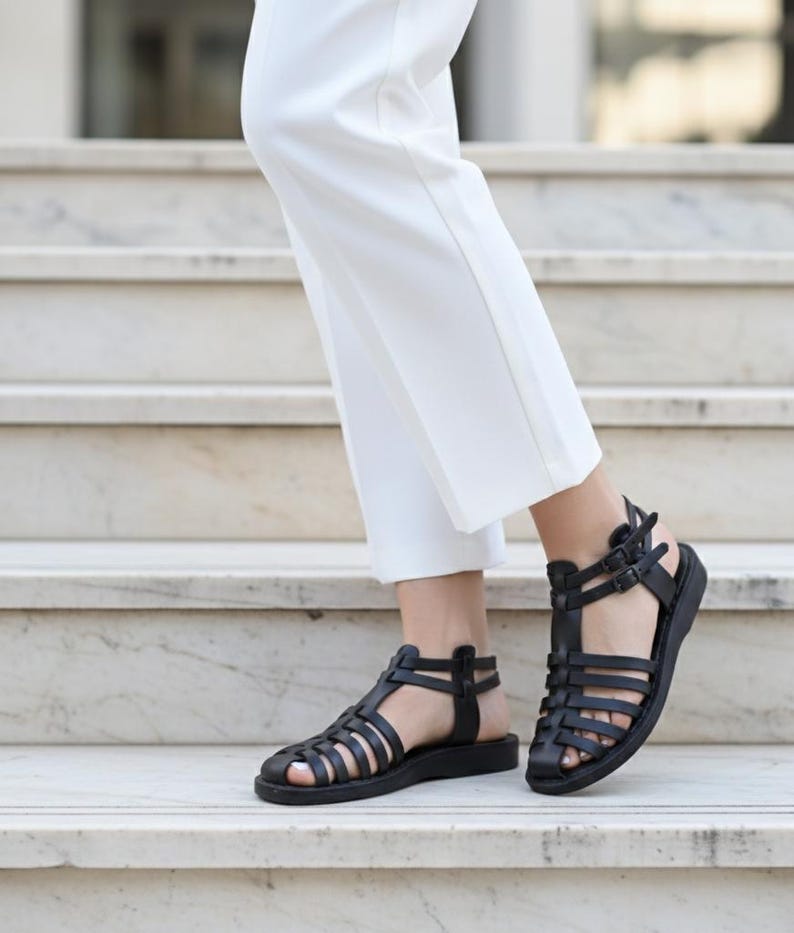 Elegant black leather gladiator sandals walking down marble stairs. Classic women's handmade summer shoes offering chic comfort for formal or casual wear.