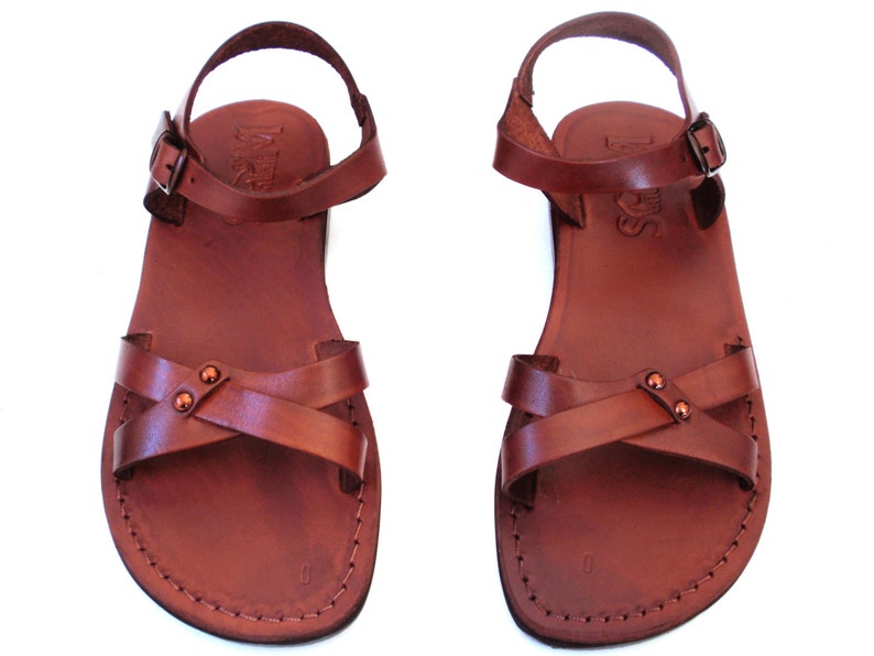 May include: A pair of brown leather sandals with a cross-strap design and adjustable ankle straps. The sandals have a stitched sole and a buckle closure. The leather appears to be a rich, reddish-brown color.