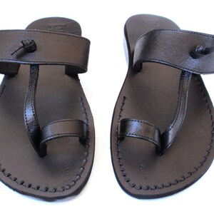 K&ouml;nnte beinhalten: Ein Paar schwarze Ledersandalen mit Zehenschlaufe und verstellbarem Riemen. Die Sandalen haben ein schlichtes Design und sind perfekt f&uuml;r warmes Wetter.