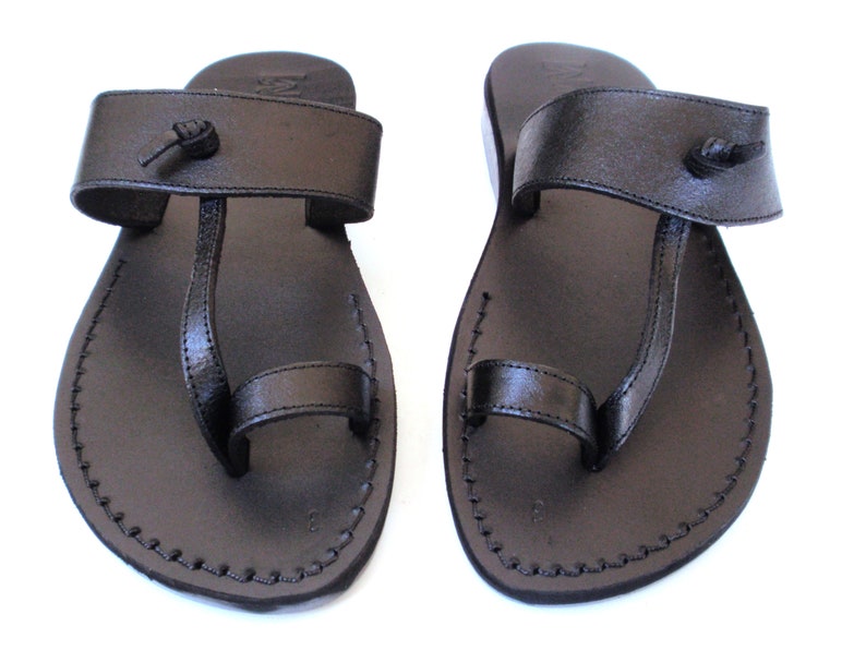 K&ouml;nnte beinhalten: Ein Paar schwarze Ledersandalen mit Zehenschlaufe und verstellbarem Riemen. Die Sandalen haben ein schlichtes Design und sind perfekt f&uuml;r warmes Wetter.