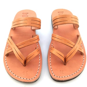 May include: A pair of tan leather sandals with criss-cross straps. The sandals have a simple design and are made of high-quality leather.