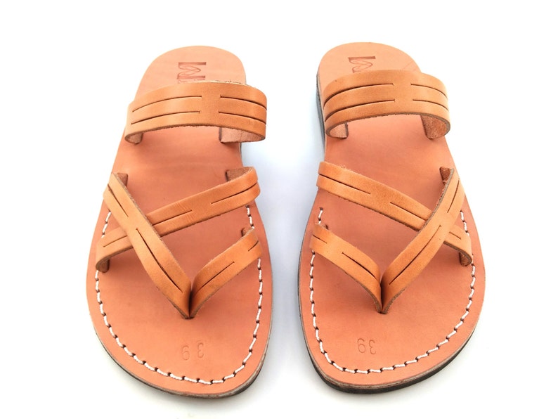 May include: A pair of tan leather sandals with criss-cross straps. The sandals have a simple design and are made of high-quality leather.