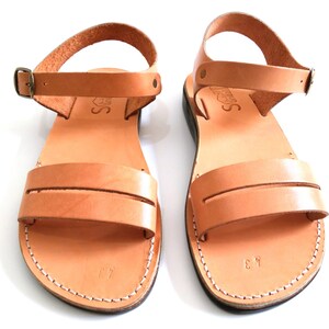 May include: A pair of tan leather sandals with a buckle fastening. The sandals have a simple design with a single strap across the foot.