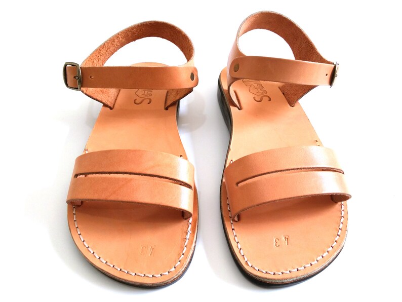 May include: A pair of tan leather sandals with a buckle fastening. The sandals have a simple design with a single strap across the foot.