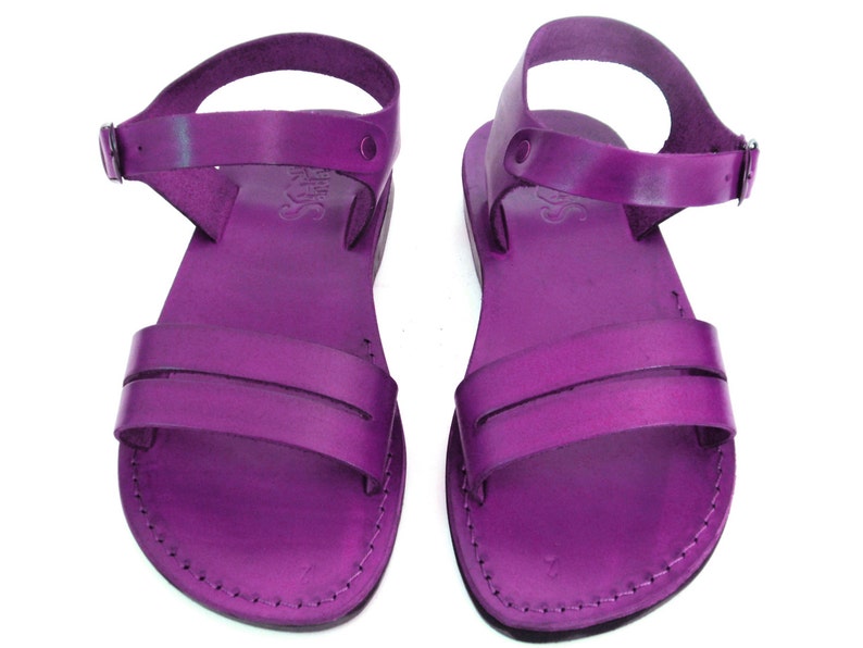 May include: A pair of purple leather sandals with an ankle strap and buckle fastening. The sandals have a simple design with a single strap across the top of the foot.