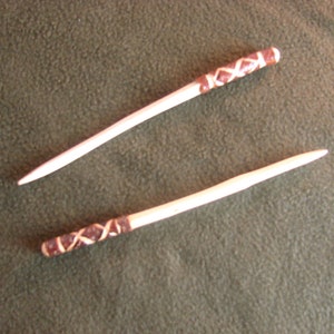 May include: Two white wooden sticks with brown leather wrappings at the top. The sticks are approximately 30 cm long.
