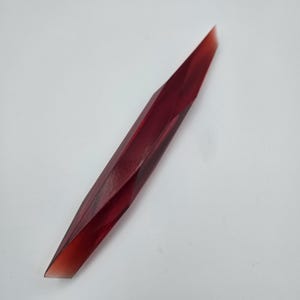 K&ouml;nnte beinhalten: Ein langes, d&uuml;nnes, rotes, facettierter Glaswerkzeug mit einer spitzen Spitze.