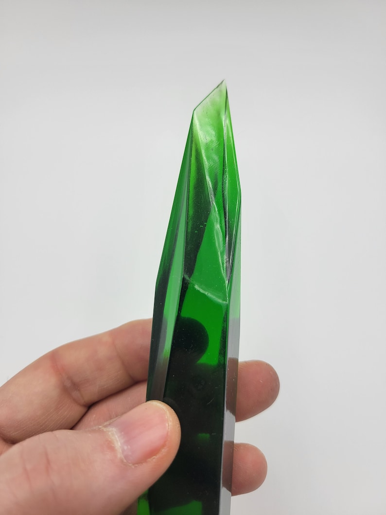 K&ouml;nnte beinhalten: Ein dunkelgr&uuml;ner Glaskristall mit einer spitzen Spitze und einer glatten, polierten Oberfl&auml;che.