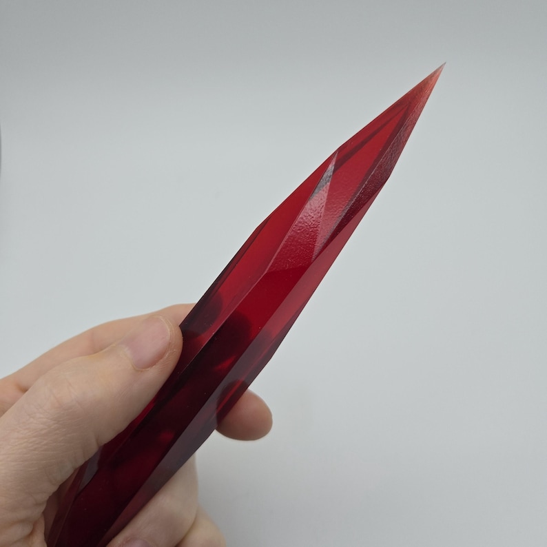 K&ouml;nnte beinhalten: Ein rotes, facettieres Messer in Kristallform mit einer scharfen Spitze.