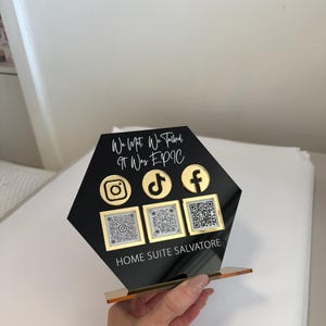 May include: Black hexagonal acrylic sign with gold trim. The sign has the text "We Met. We Talked. It Was EPIC" and features social media icons for Instagram, TikTok, and Facebook. There are also QR codes for each platform. The sign reads "Home Suite Salvatore" at the bottom.