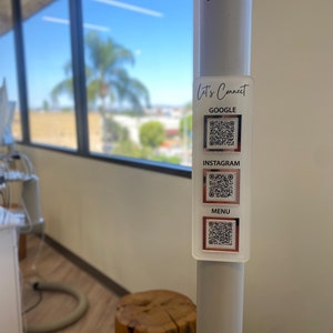May include: A white pole with a sticker that says "Let's Connect" and has three QR codes labeled "Google", "Instagram", and "Menu".